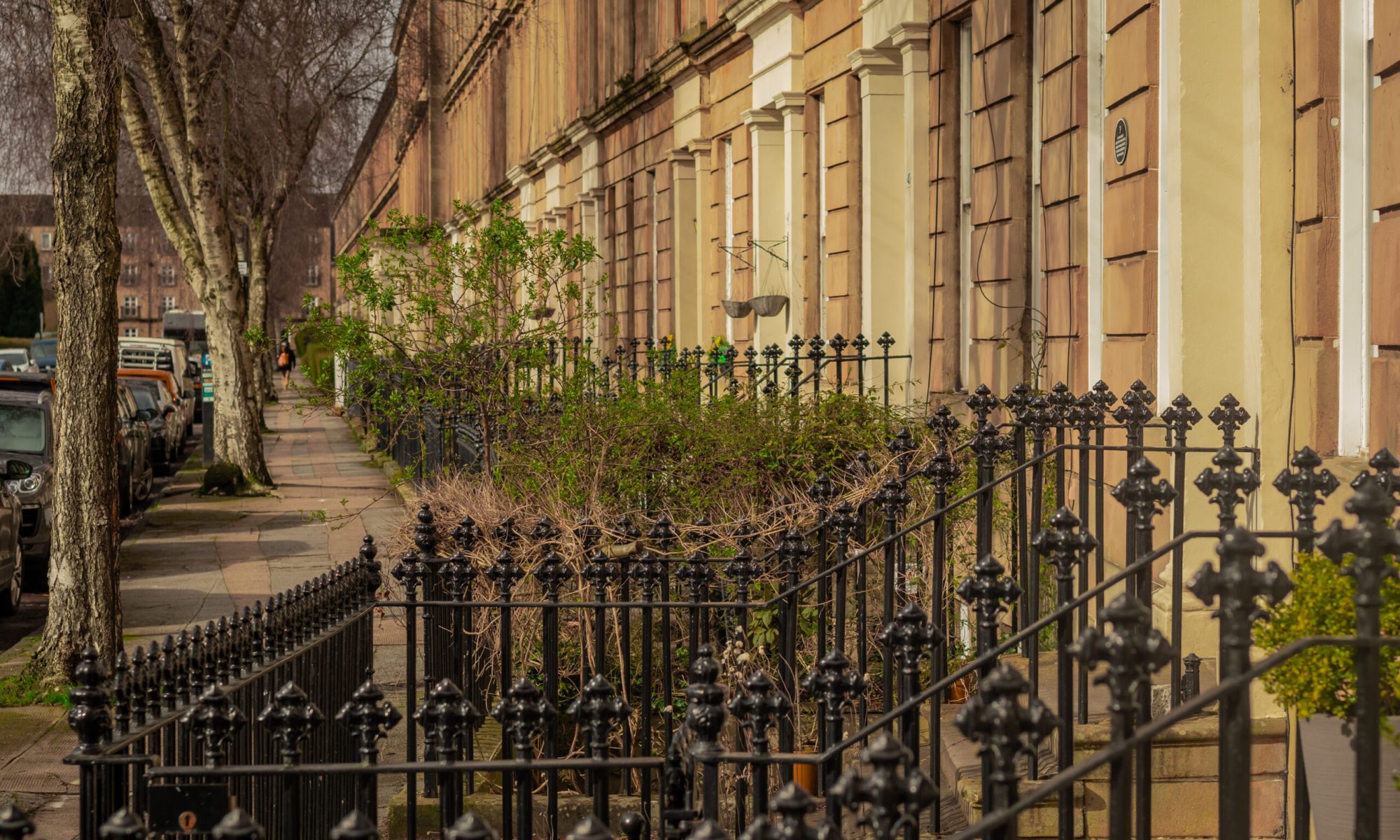 Typical street in the suburb of Glasgow, a row of older type houses holding together in one long building with metal fence in the front.